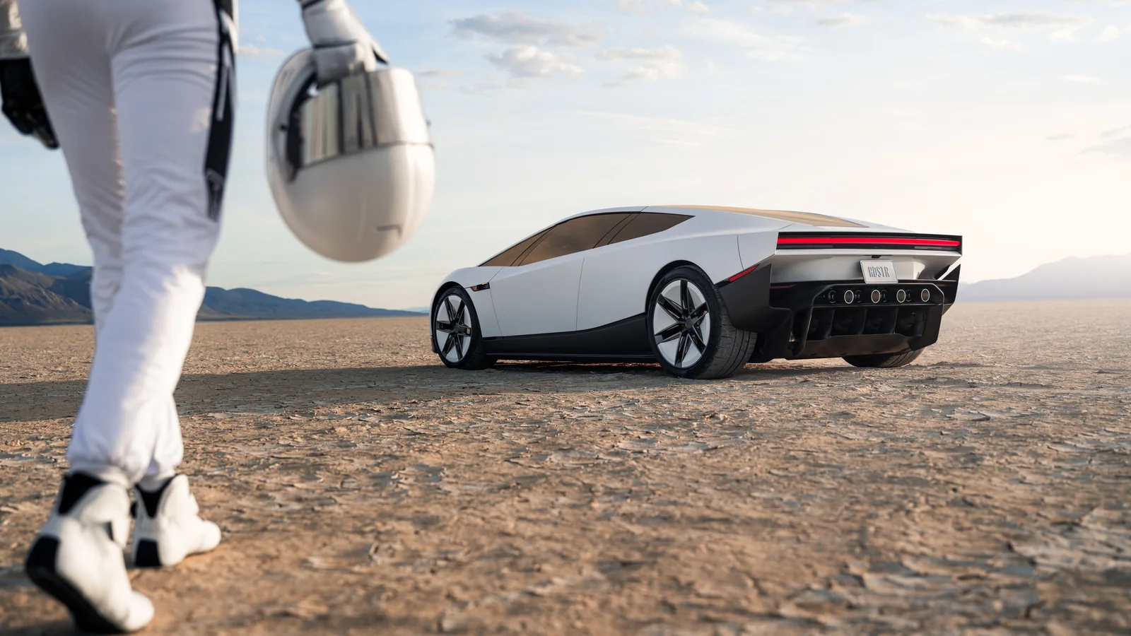 A man in white pants walks in the foreground while a Tesla Roadster sits on open desert terrain.