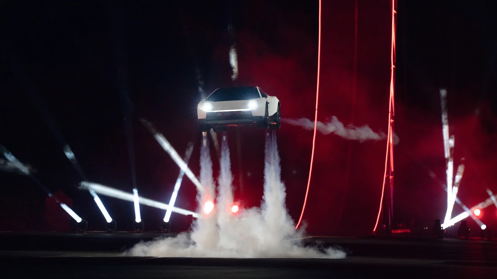 Tesla Roadster hovering above a stage during the reveal, amid smoke and red lighting.